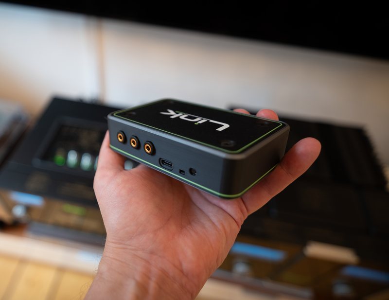 Link held in one hand, a hi-fi rack out of focus behind it